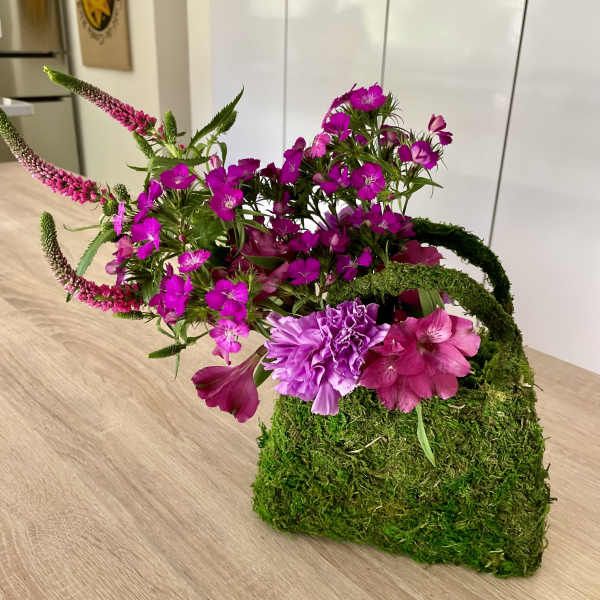 Pink and purple flowers arranged in a moss-covered container