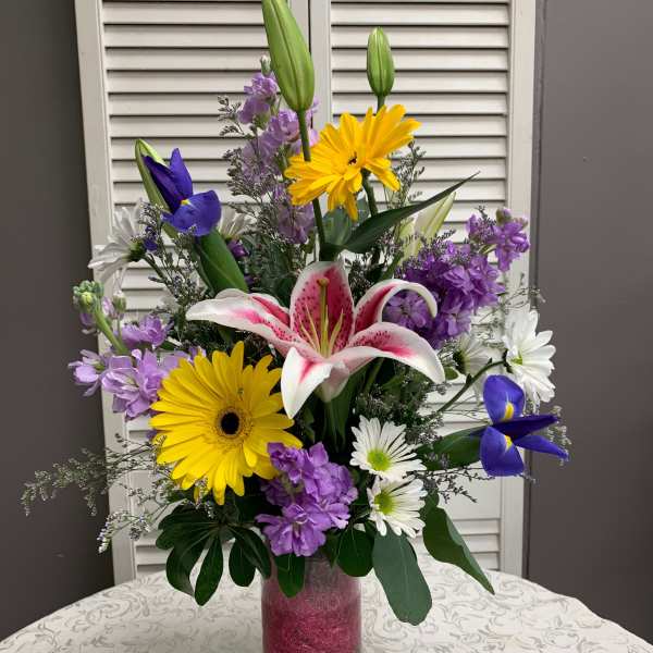 Mixed bouquet of lilies, daisies, and purple flowers in a tall glass vase