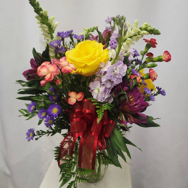Mixed bouquet with a yellow rose in a glass vase and red ribbon