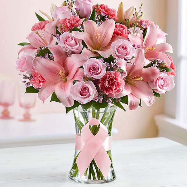 Pink lilies and roses arranged in a clear glass vase with a pink ribbon
