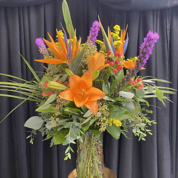 Tall tropical bouquet with orange lilies in a glass vase