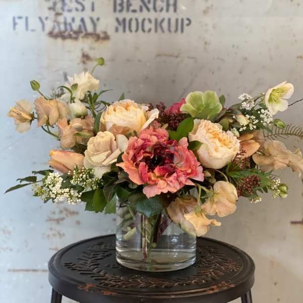 Mixed bouquet of peach, pink, and white flowers in a clear glass vase