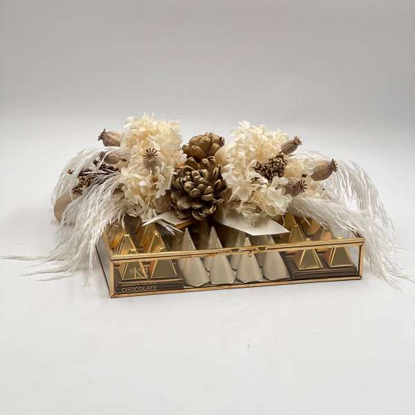 Cream floral arrangement on a gold chocolate box with feather accents