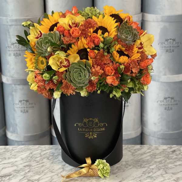 Bouquet of sunflowers, orange roses, and succulents in a black hatbox