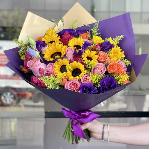 Bouquet of sunflowers and roses wrapped in purple paper