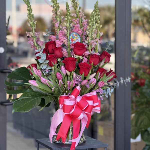 Bouquet of red roses and pink tulips in a glass vase with a pink ribbon