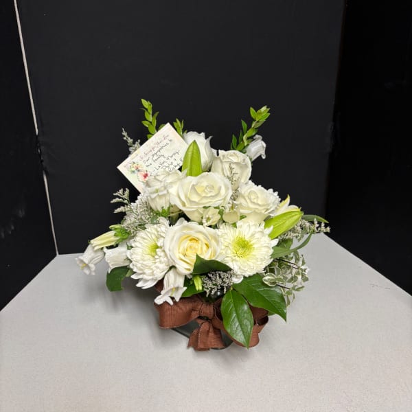 White rose and lily bouquet in a low container with a brown ribbon