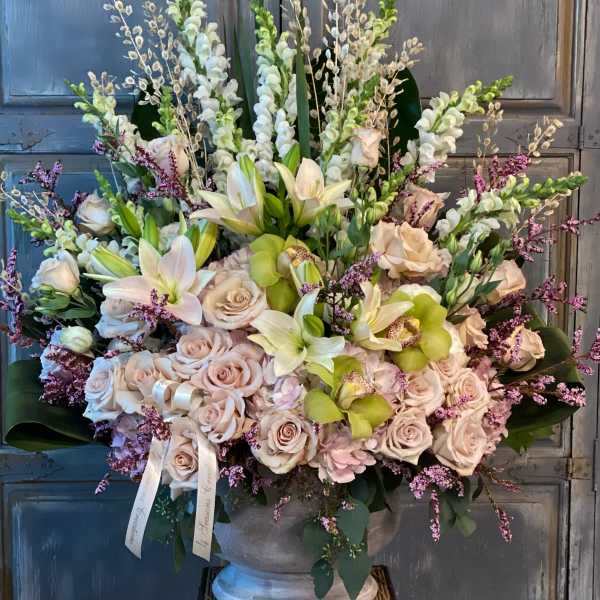 Large floral arrangement with pale roses, lilies, and orchids in a pedestal vase