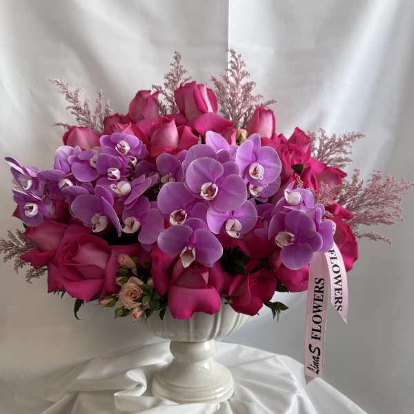 Pink roses and purple orchids arranged in a white pedestal vase