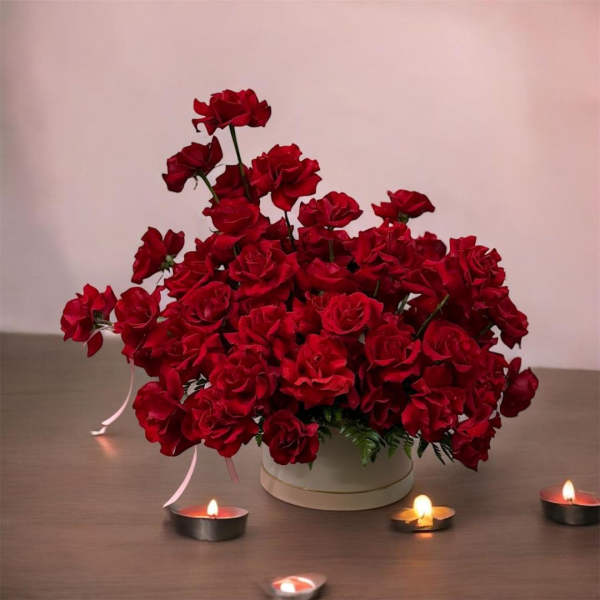 Red rose arrangement in a white round box with small candles nearby
