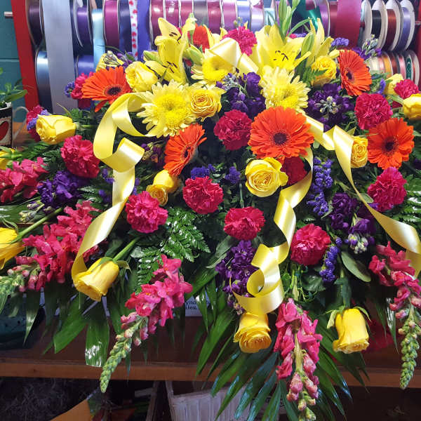 Large colorful floral casket spray with yellow, pink, purple, and orange blooms