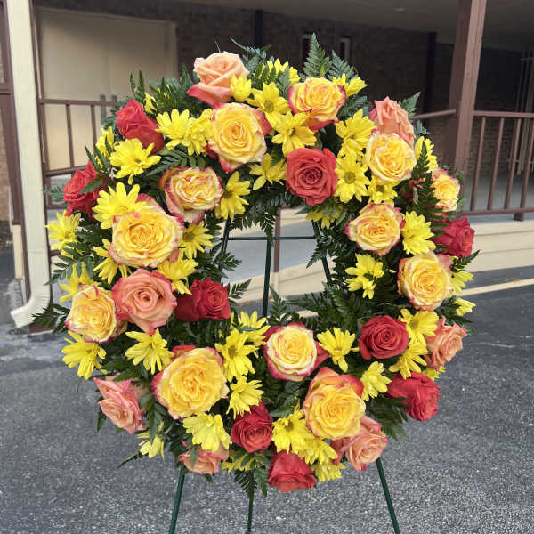 Circular wreath of yellow daisies and multicolored roses on a stand