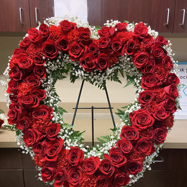 Heart-shaped red rose wreath on a stand with white filler flowers