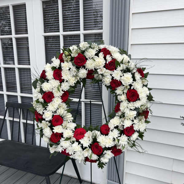 Red roses and white chrysanthemums arranged in a large wreath on a stand