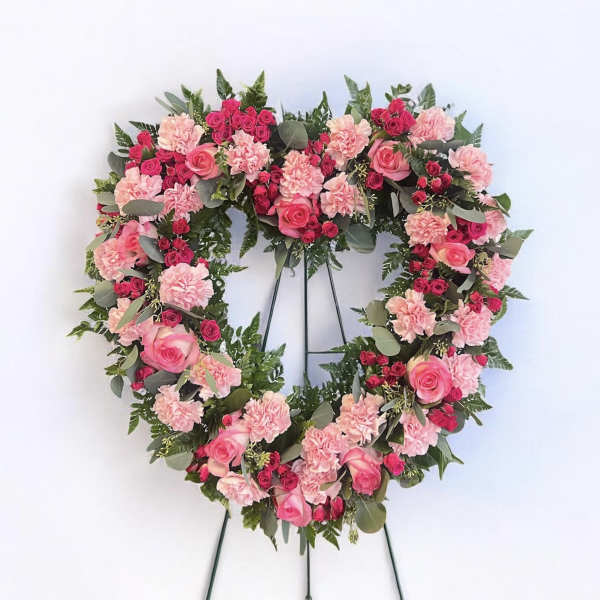 Heart-shaped floral wreath with pink roses and carnations on a stand