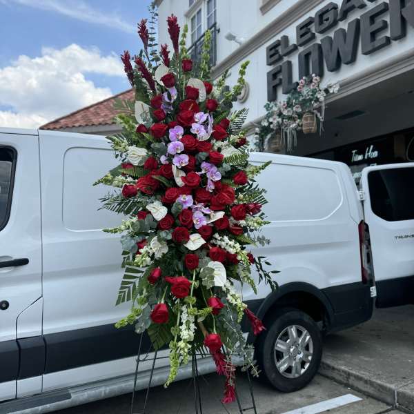 Tall standing floral spray with red roses and purple orchids on an easel