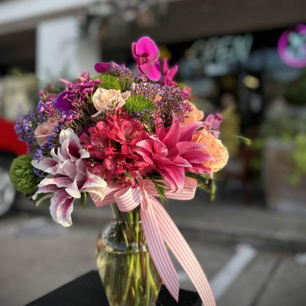 Bright mixed bouquet in a glass vase with a pink striped ribbon