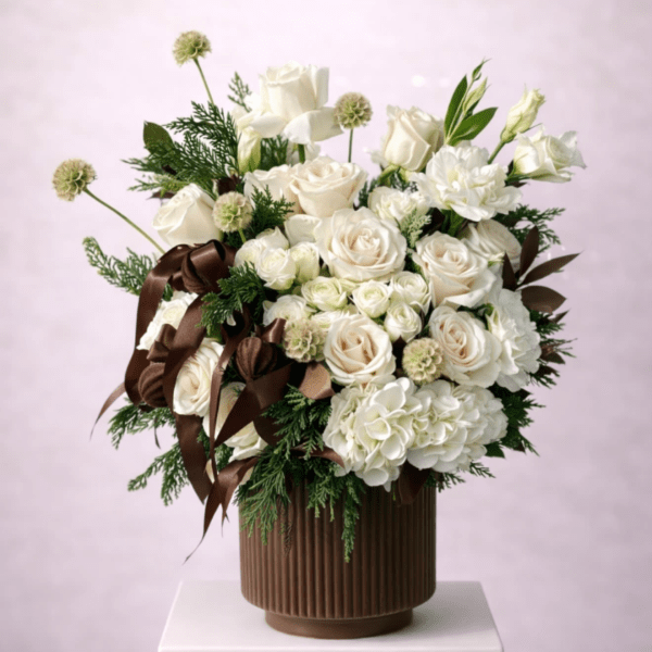 White rose arrangement in a brown ribbed vase with dark ribbon accents