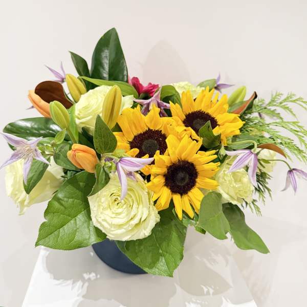 Bouquet of sunflowers, white roses, and lilies in a dark vase