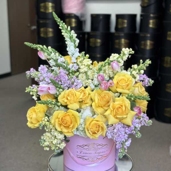 Yellow roses and lavender flowers arranged in a pink hat box