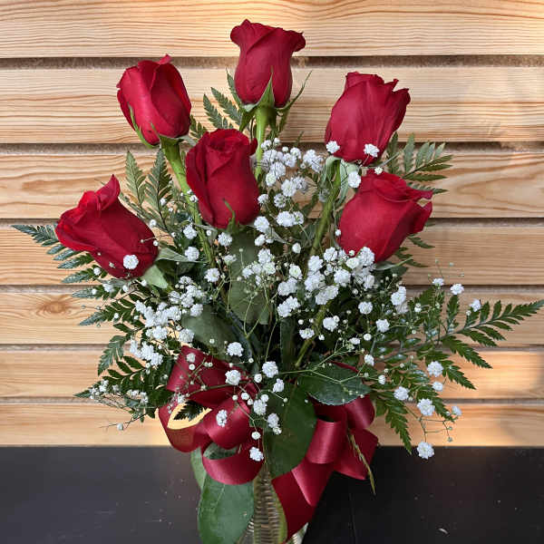 Red roses arranged in a clear vase with white baby's breath and a red ribbon