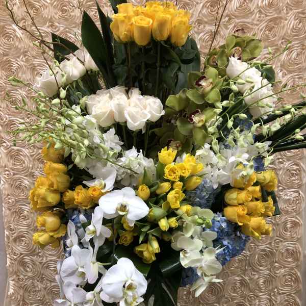 Tall bouquet of yellow roses, white orchids, and blue hydrangeas in a clear vase