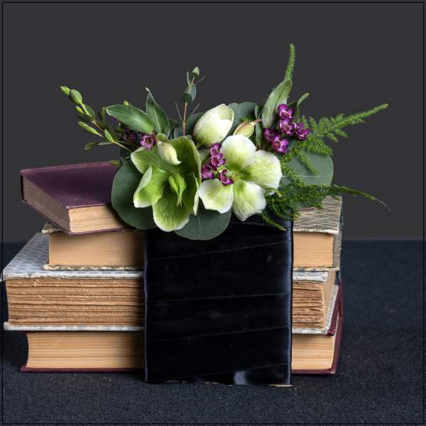 Green and white flowers in a black ribbon wrap on stacked books