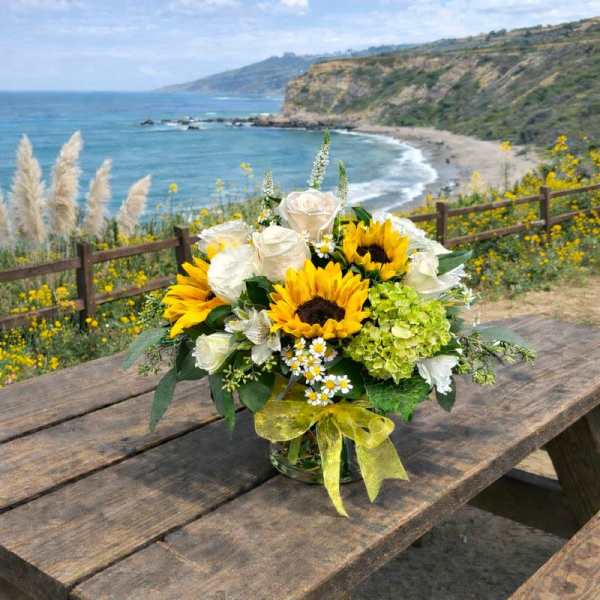 Bouquet of sunflowers and white roses in a glass vase with a yellow ribbon