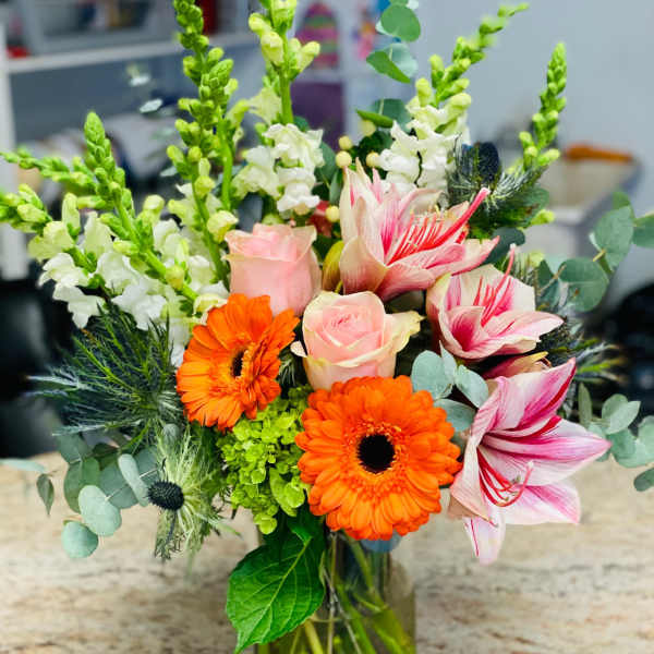 Mixed bouquet with orange gerbera daisies, pink roses, and striped lilies in a glass vase