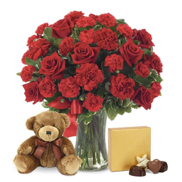 Red rose and carnation bouquet in a glass vase with a teddy bear and chocolates