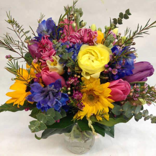 Colorful mixed bouquet in a clear glass vase with sunflowers and tulips
