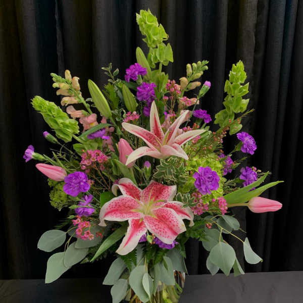 Tall bouquet of pink lilies and purple flowers in a glass vase