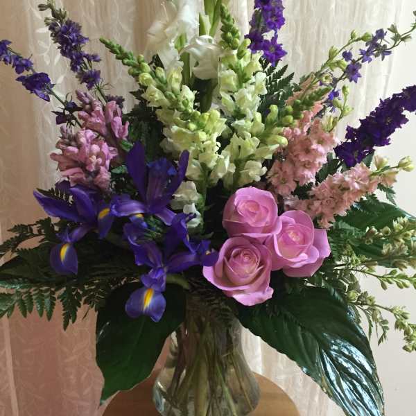 Mixed bouquet with pink roses, purple irises, and tall white and lavender spikes in a glass vase
