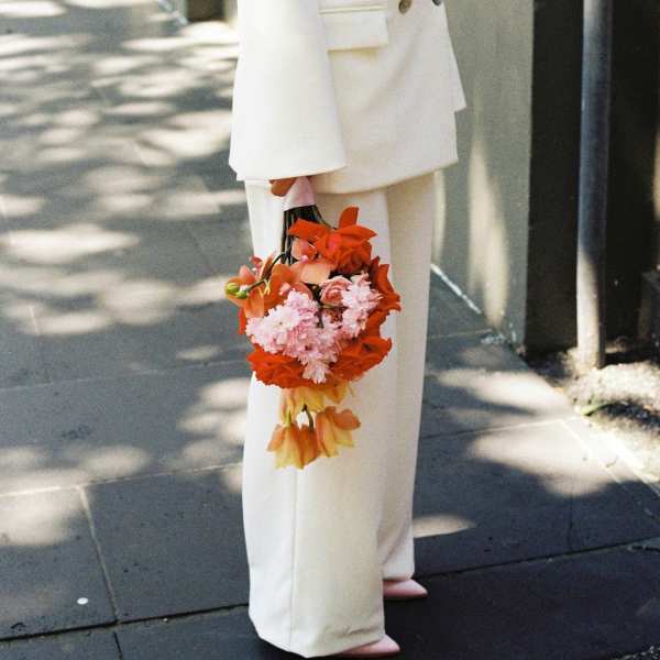 Person in white suit holding a colorful bouquet of pink and orange flowers