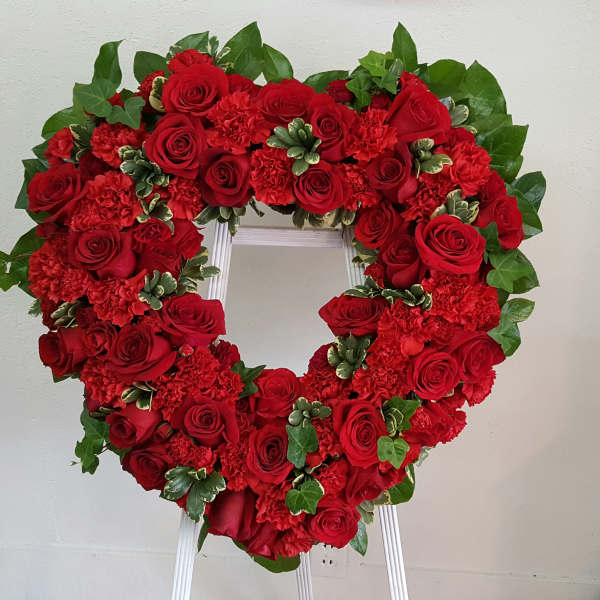 Heart-shaped wreath of red roses and carnations on a white stand