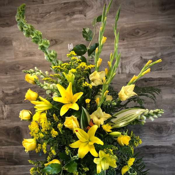 Tall yellow floral standing spray with lilies and roses on a black easel