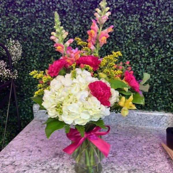 Bouquet of white and pink flowers in a glass vase with a pink ribbon