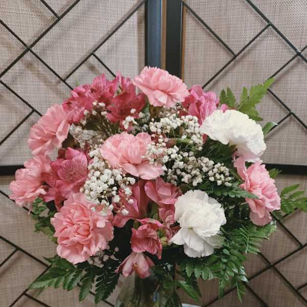 Pink and white bouquet in a glass vase with a small figurine beside it