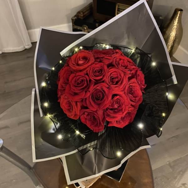 Bouquet of red roses wrapped in black paper with small lights