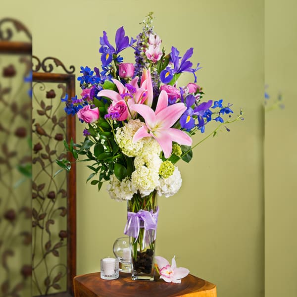 Tall bouquet of pink lilies, roses, and blue irises in a glass vase