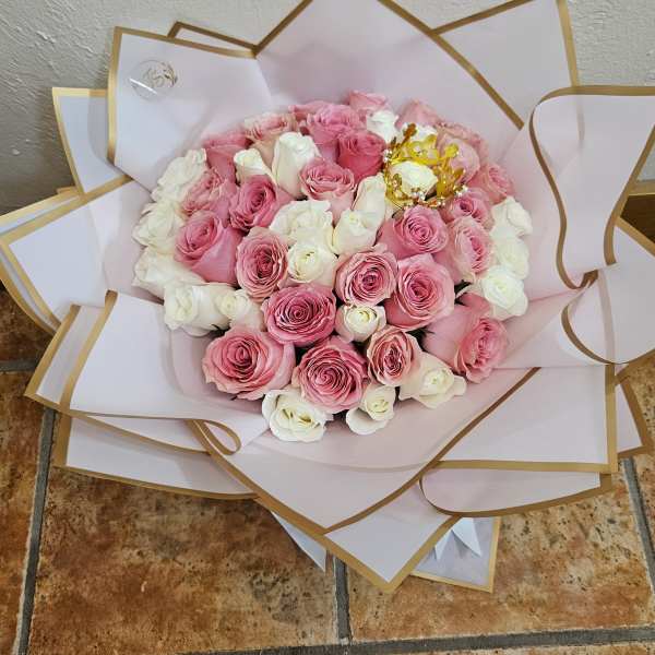 Bouquet of pink and white roses wrapped in white paper with gold trim