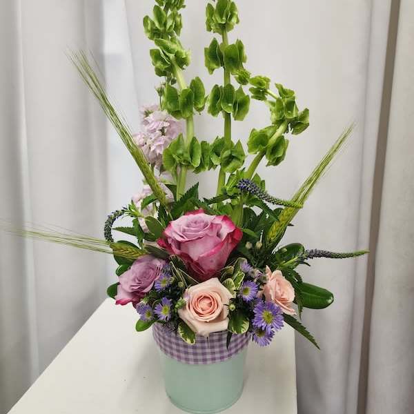 Tall floral arrangement with pink and lavender roses in a mint container