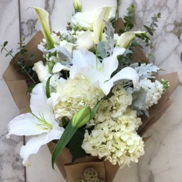White lily and hydrangea bouquet wrapped in brown paper with a white ribbon