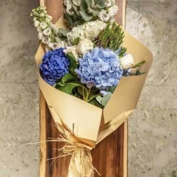 Bouquet of blue hydrangeas and white flowers wrapped in tan paper