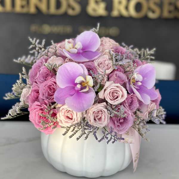 Pink roses and lavender orchids arranged in a white pumpkin vase