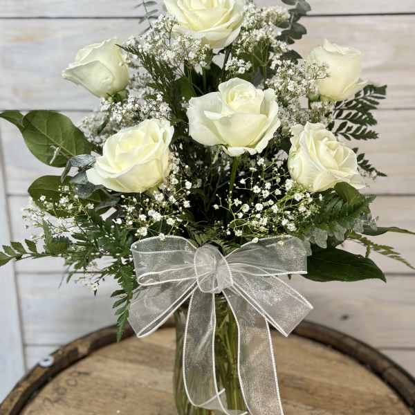 White roses in a glass vase with baby's breath and a silver ribbon