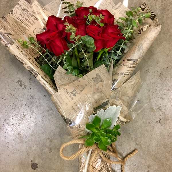 Bouquet of red roses wrapped in newspaper-style paper with eucalyptus and a succulent accent