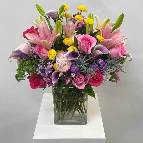 Mixed bouquet of pink lilies, roses, and purple flowers in a glass vase