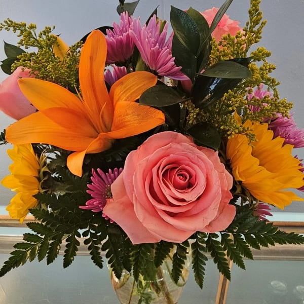 Pink rose and orange lily arrangement in a glass vase