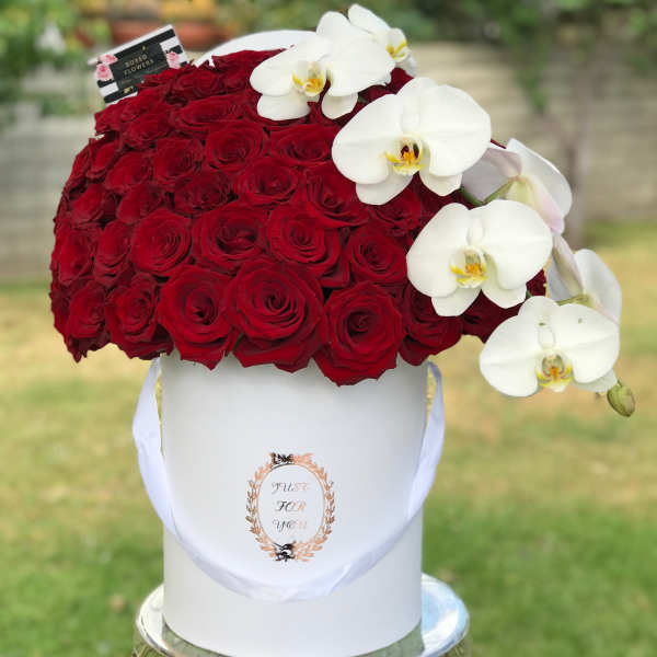 Red roses in a white hatbox with white orchids draped over the side